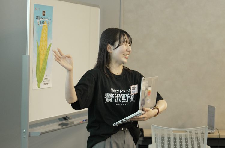 「贅沢野菜®」のTシャツを着て、スーパースイートコーンのこだわりを紹介する商品担当者
