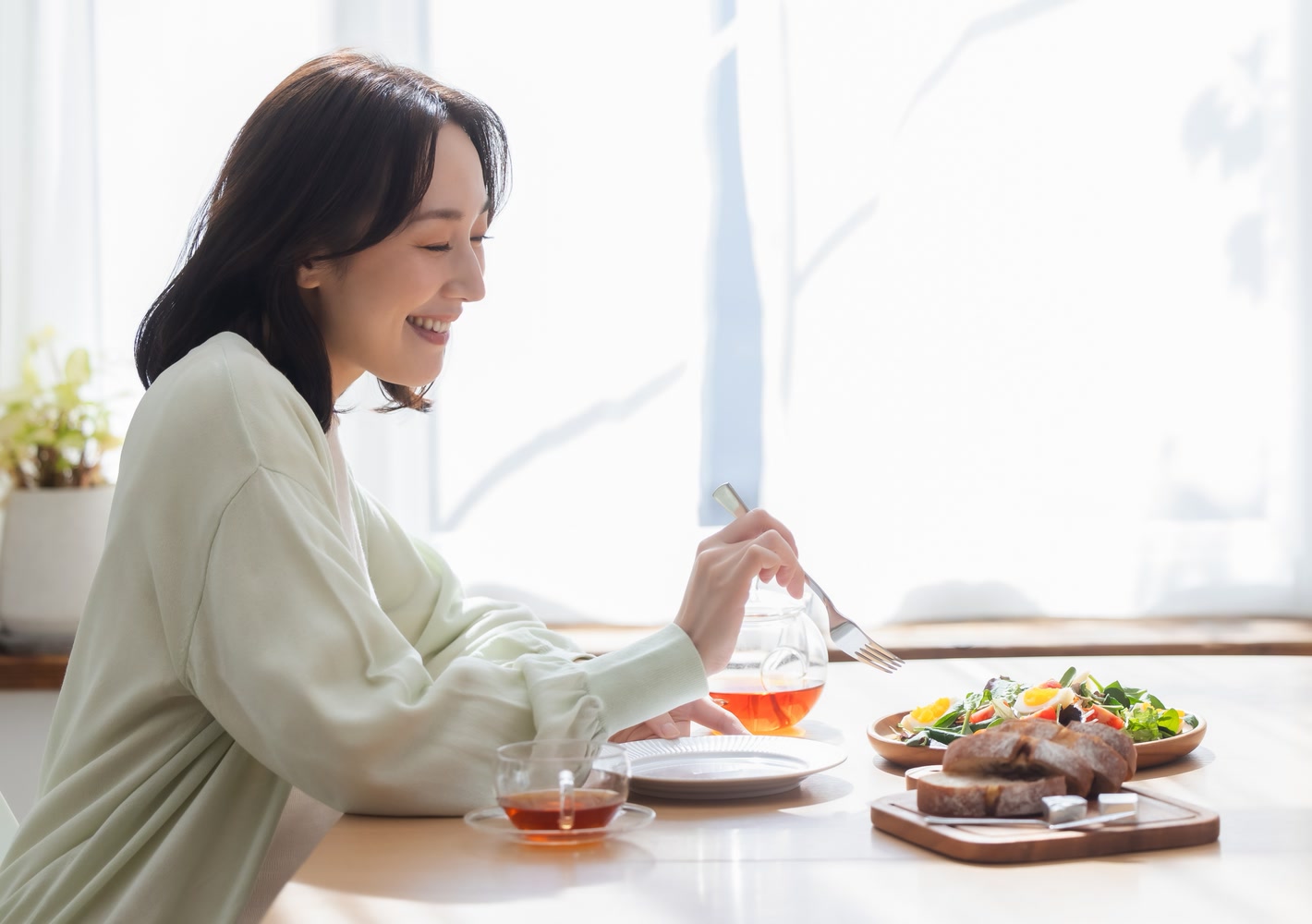 窓辺の明るい食卓で食事を楽しむ女性